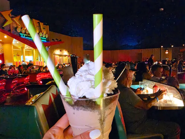 A milkshake held up in front of the car booths at the Sci-Fi Dine-In Theater