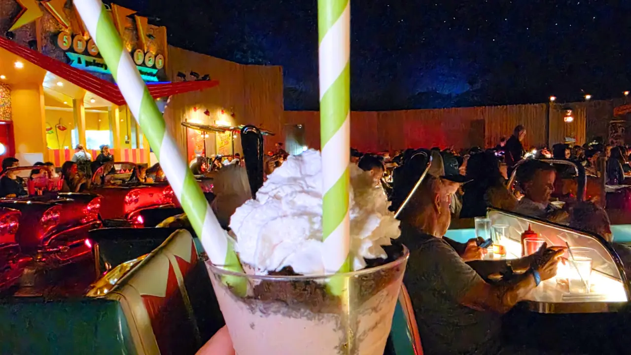 A milkshake held up in front of the car booths at the Sci-Fi Dine-In Theater