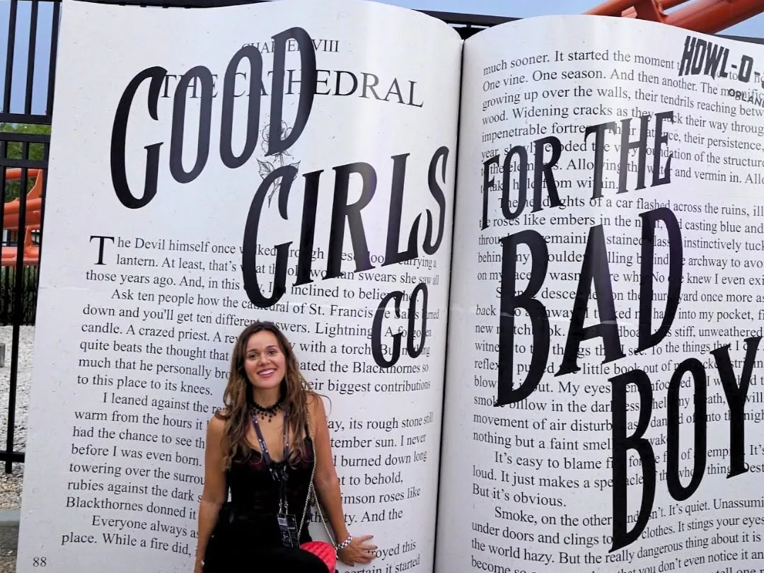 Kaleigh crouching in front of a giant open book photo op reading Good Girls Go for the Bad Boy at Howl-O-Scream